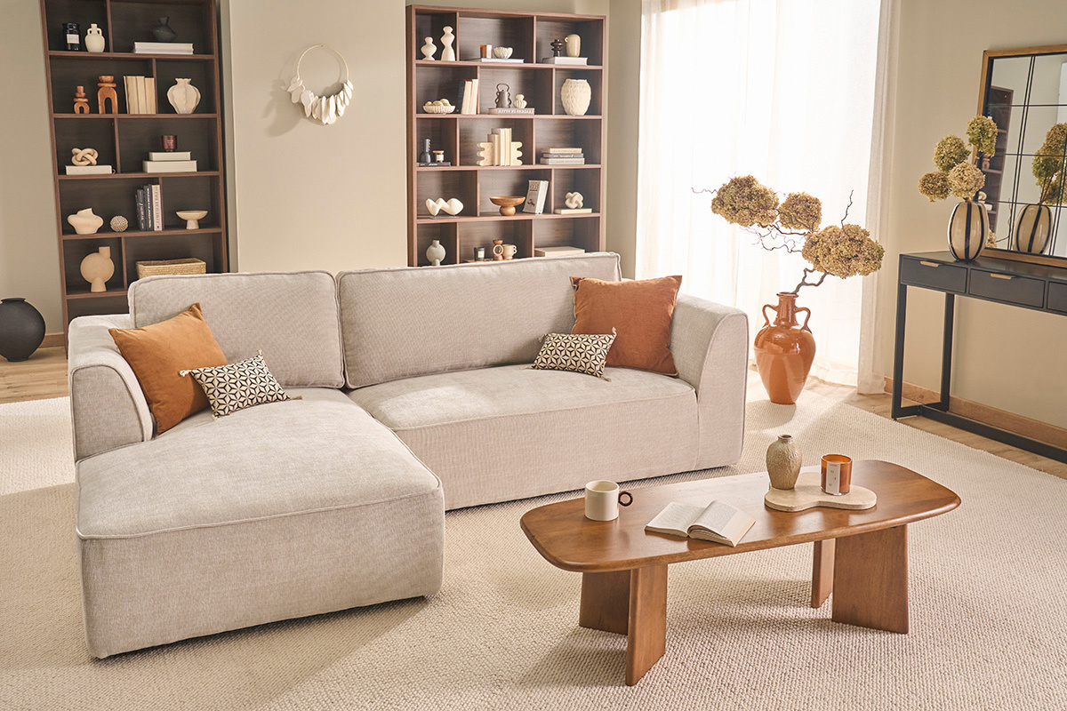 Canap� d'angle gauche beige en tissu effet velours 3 places, vue de 3/4, avec table basse et d�corations.