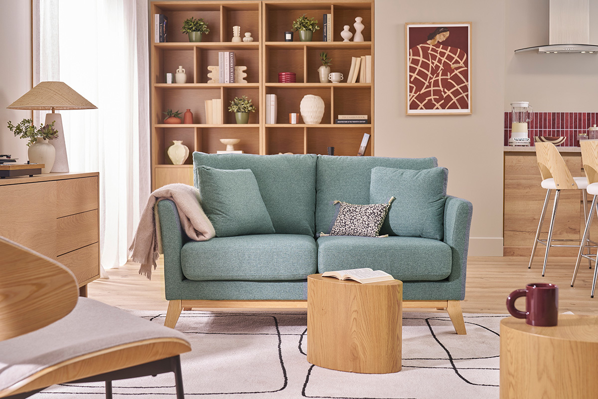 Canap� 2 places en tissu vert de gris et bois clair avec coussins, vue de face dans un salon.