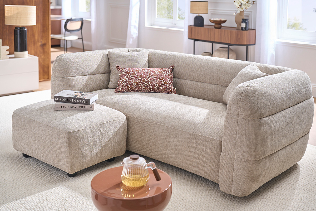 Pouf repose pieds en tissu beige JOYA, � c�t� d'un canap�, vue d'ensemble en int�rieur lumineux.